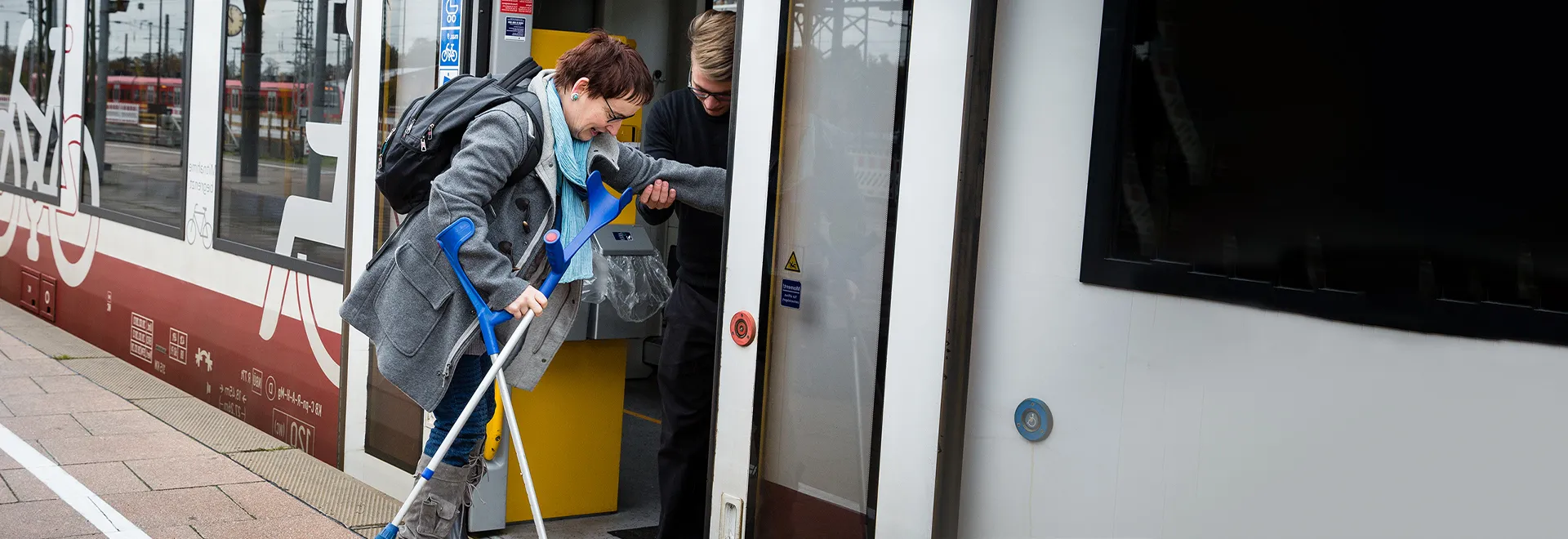 Eine Frau mit einer Gehbehinderung steigt in eine Regionalbahn ein.