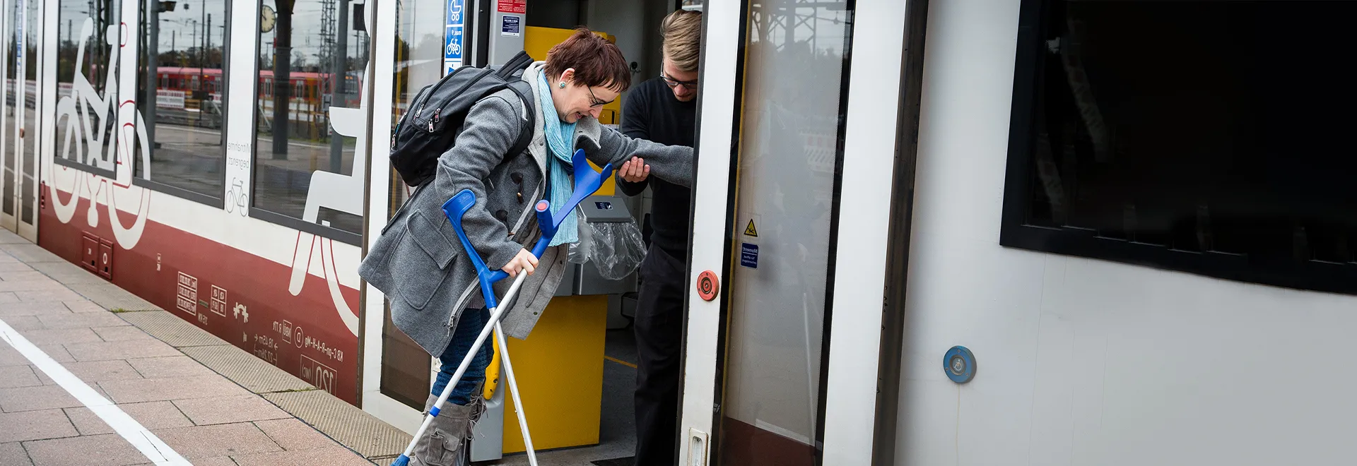 Eine Frau mit einer Gehbehinderung steigt in eine Regionalbahn ein.