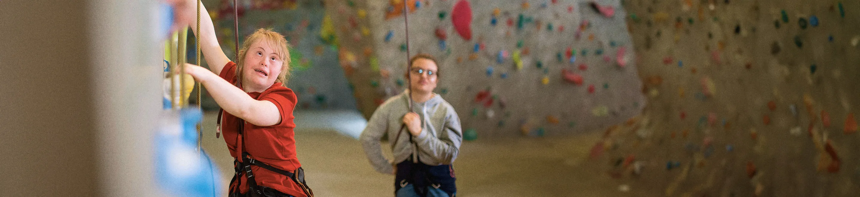 Eine junge Frau mit dem Down-Syndrom beim Klettern in der Kletterhalle.