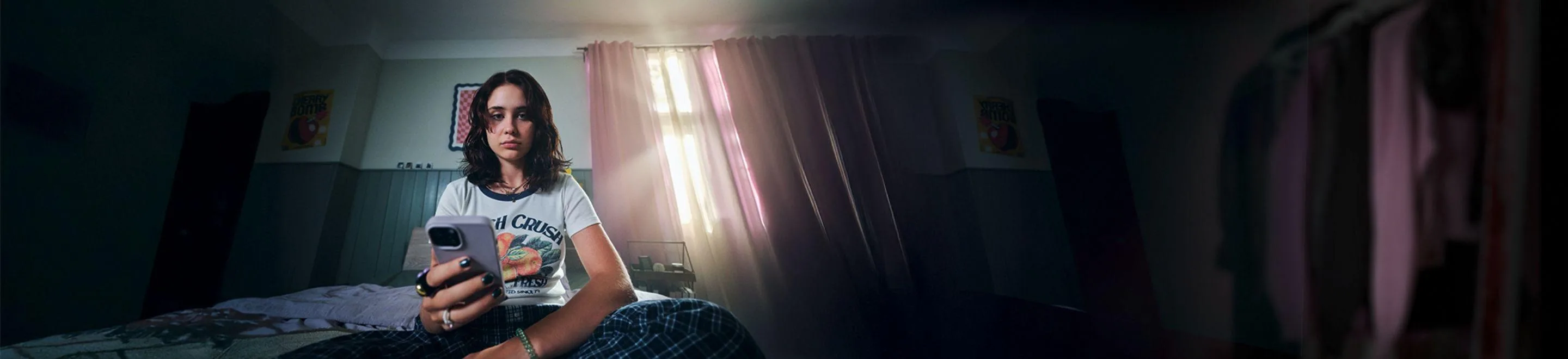 Eine Jugendliche sitzt in einem Zimmer auf dem Bett und guckt auf ihr Smartphone.