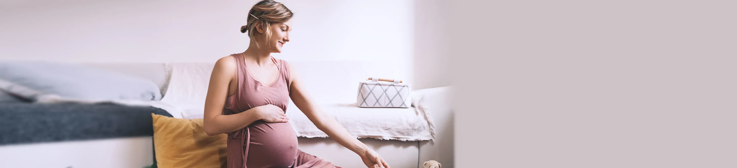 Eine schwangere Frau sitzt auf dem Boden und sortiert Babysachen.