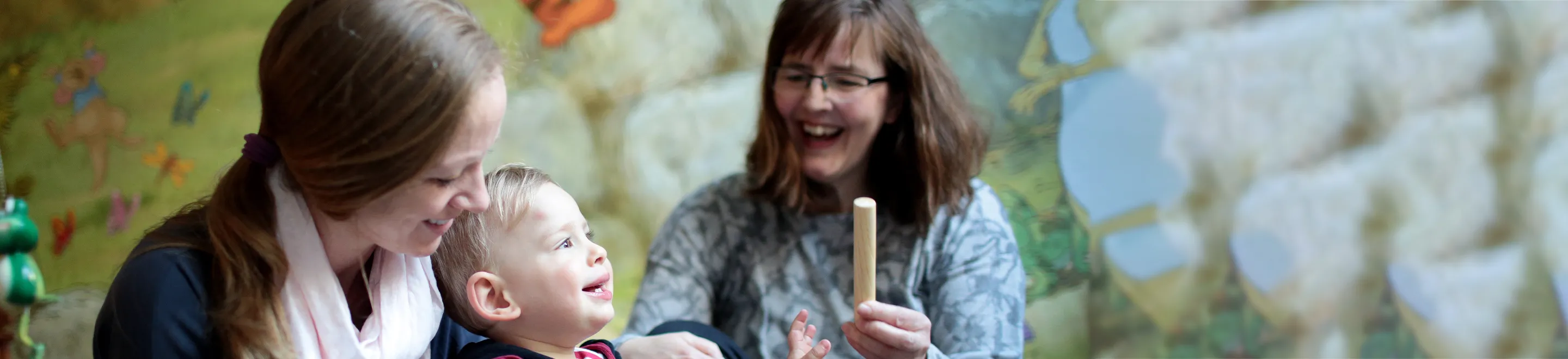 Ein Kind spielt mit Holzspielzeug, zwei Frauen spielen mit.