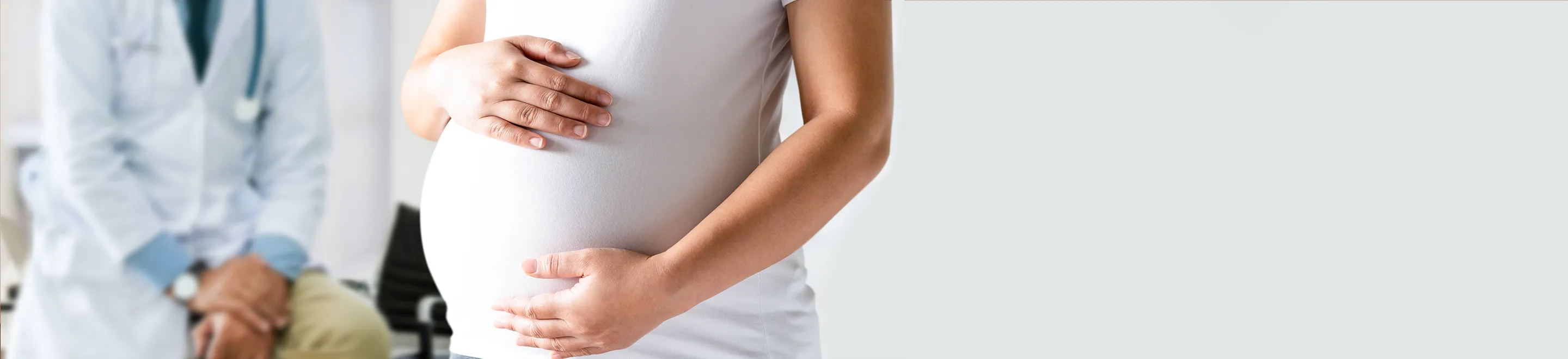 Eine schwangere Frau hält die Hände auf ihrem große Bauch, im Hintergrund sitzt ein Arzt.