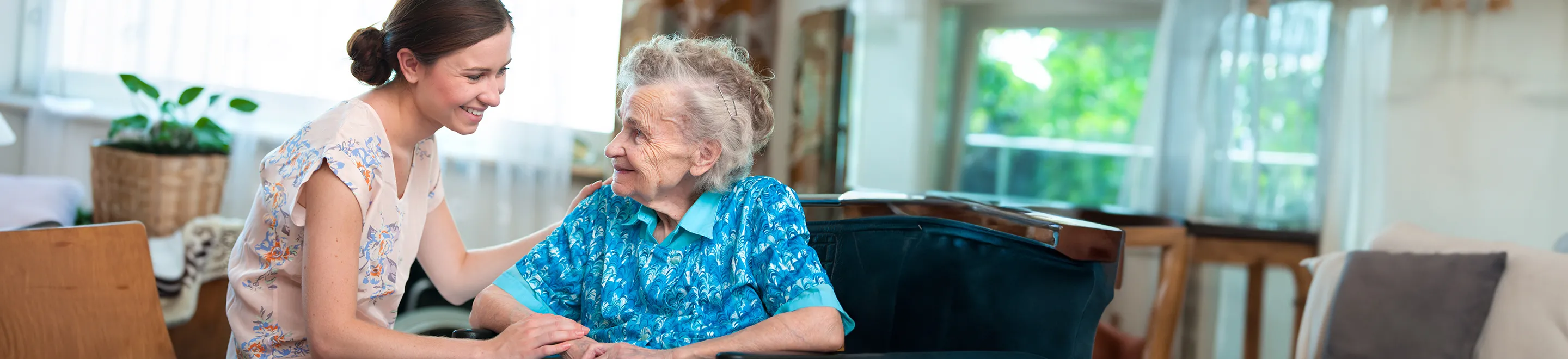 Eine Seniorin sitzt im Sessel neben einer jungen Frau.