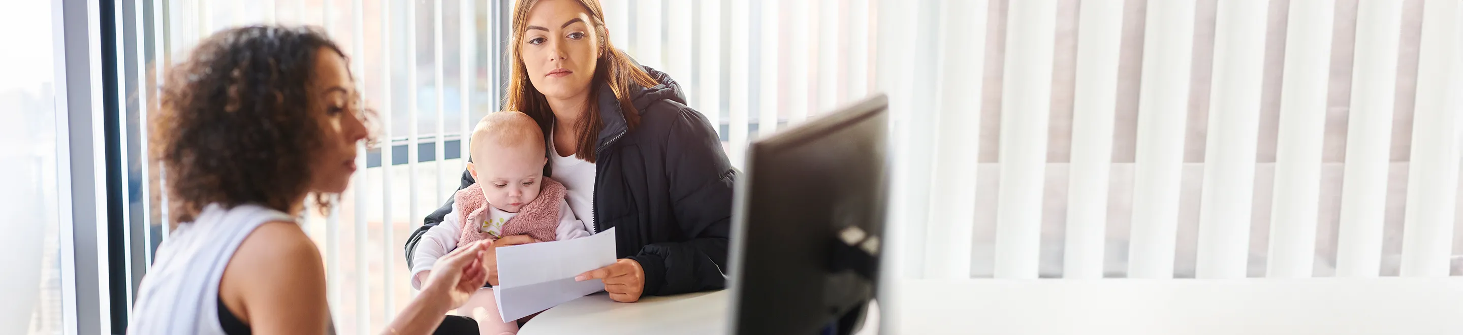 Eine Frau mit Baby sitzt  neben einer Frau am Computer-Bildschirm.