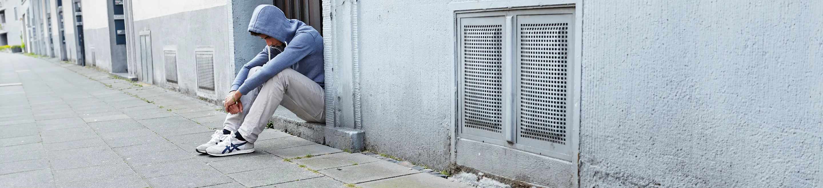 Ein Jugendlicher mit Kapuzenpulli sitzt traurig am Straßenrand
