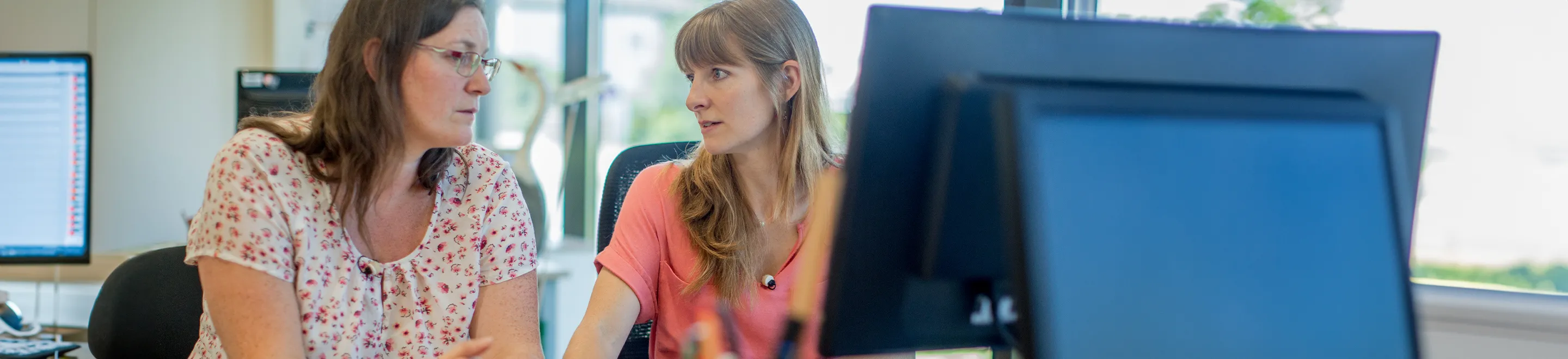 Zwei Frauen im Gespräch vor einem PC-Bildschirm.