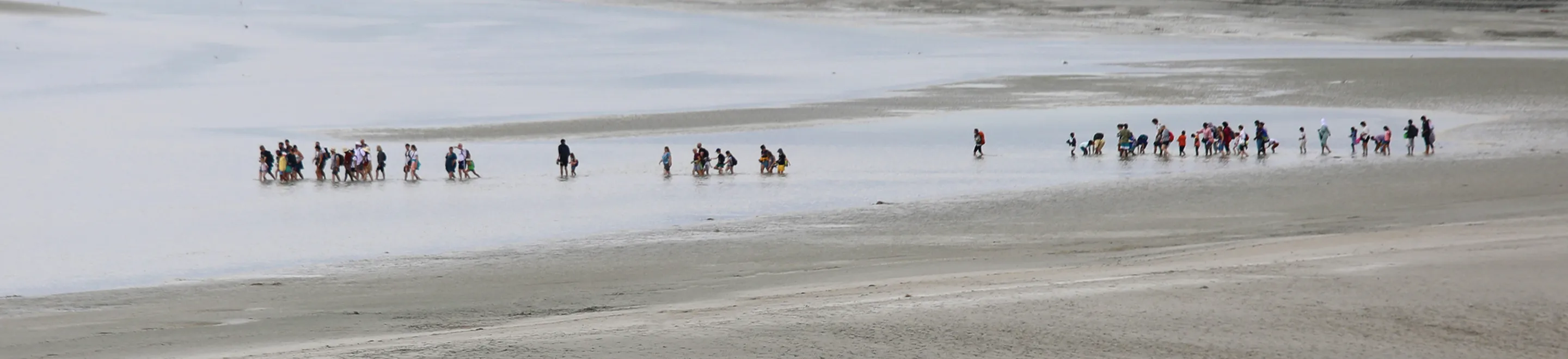 Eine Gruppe von Menschen, die in einer Entfernung durch ein Gewässer waten.
