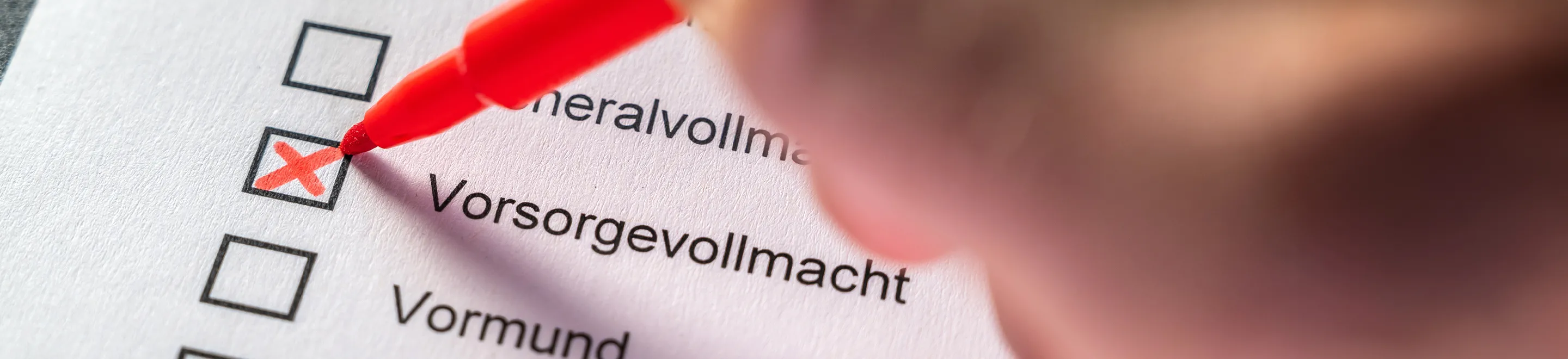 Eine Hand kreuzt mit einem roten Stift auf einer Checkliste das Wort "Vorsorgevollmacht" an.