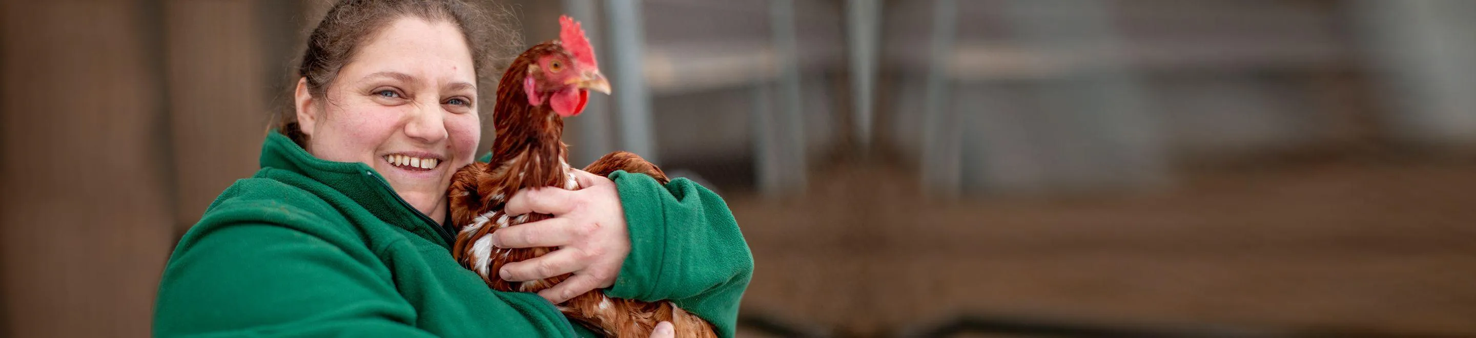 Eine lächelnde Frau hält ein Huhn im Arm.