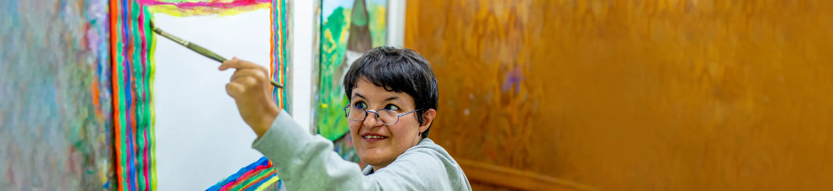 Eine Frau malt mit einem Pinsel und bunten Farben ein Bild.