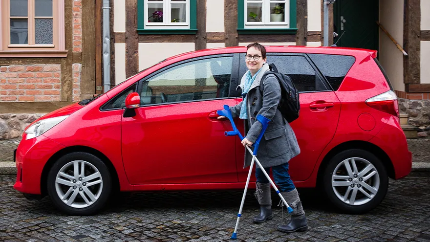 Eine Frau mit Krücken steht vor einem Auto.
