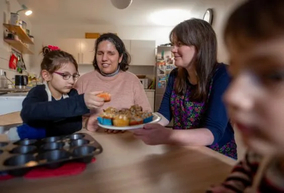 Eine blinde Frau mit Ihren Kindern und eine Frau ohne Behinderung sitzen an einem Küchentisch.