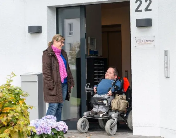 Eine Frau und ein Mann im Rollstuhl vor einem Gebäude.