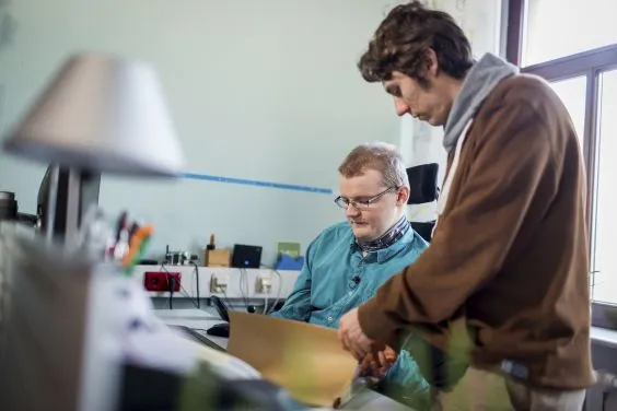 Ein Assistent hilft einem Mann mit Behinderung bei der Arbeit.