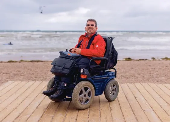 Ein Mann im Rollstuhl am Strand, im Hintergund das Meer