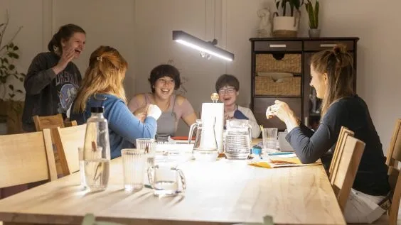Eine Gruppe junger Menschen sitzt am Tisch, sie sprechen miteinander und lachen