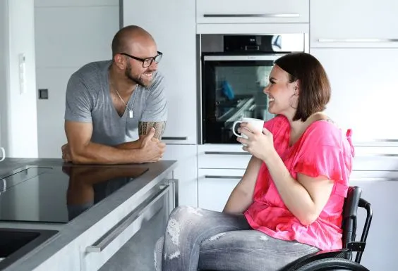 Eine junge Frau im Rollstuhl und ein junger Mann unterhalten sich in einer Küche
