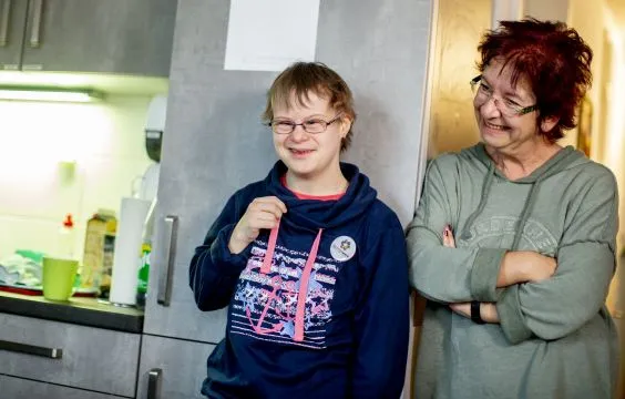 Eine Frau und ein junger Mann mit Downsyndrom stehen in einer Küche