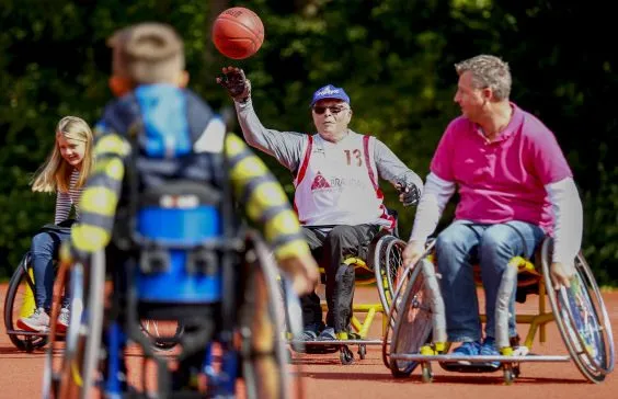 Eine Gruppe von jüngeren und älteren Menschen spielen Rollstuhl-Basketball