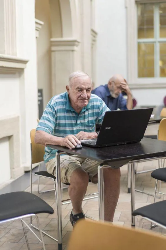 Ein älterer Mann sitzt in der Uni vor einem Computer.