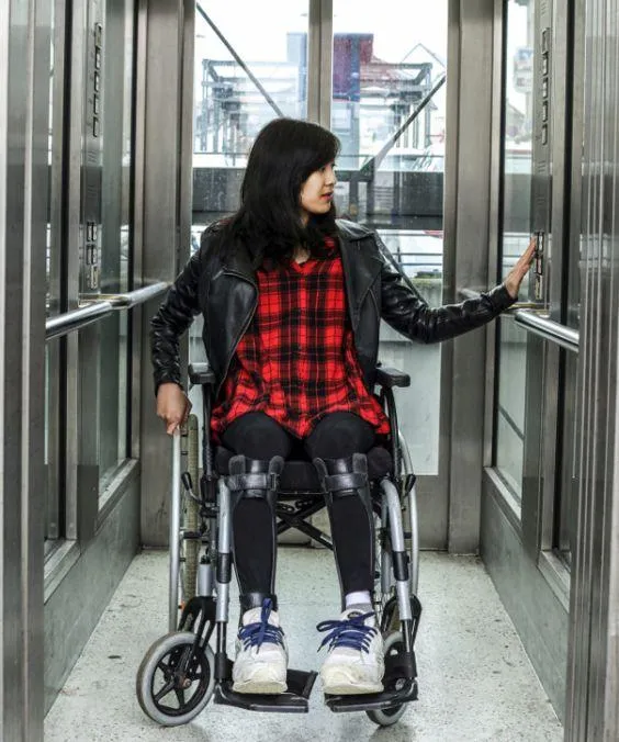 Eine Frau im Rollstuhl, in einem Aufzug.