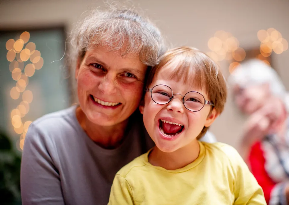 Eine Frau und ein Kind mit Downsyndrom halten lächelnd ihre Köpfe aneinander.