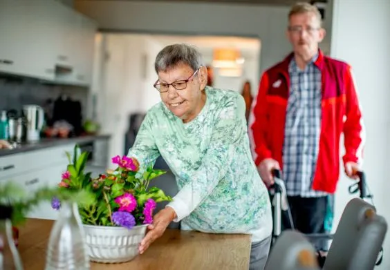 Eine ältere Frau stellt eine Blumenvase auf einen Küchentisch.