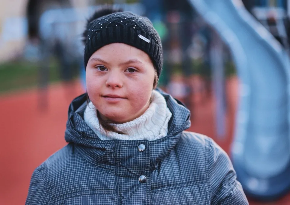 Eine junge Frau mit Downsyndrom schaut ernst in die Kamera.