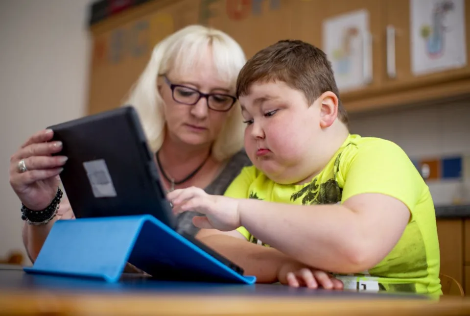 Eine Mutter und ihr Sohn schauen beide auf ein Tablet, der Junge tippt etwas.