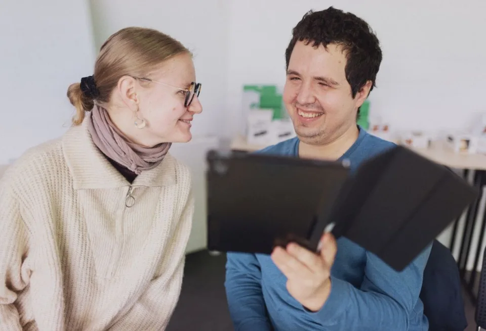 Eine Frau schaut einen Mann an, der Mann hält ein Tablet in der Hand und lächelt.