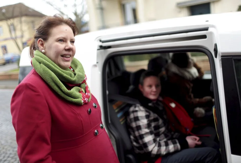 Eine Frau steht vor einer geöffneten Schiebetür eines PKWs. In dem Auto sitzen Kinder.