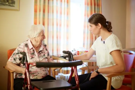 Eine junge Pflegerin sitzt mit einer Seniorin an einem Tisch.