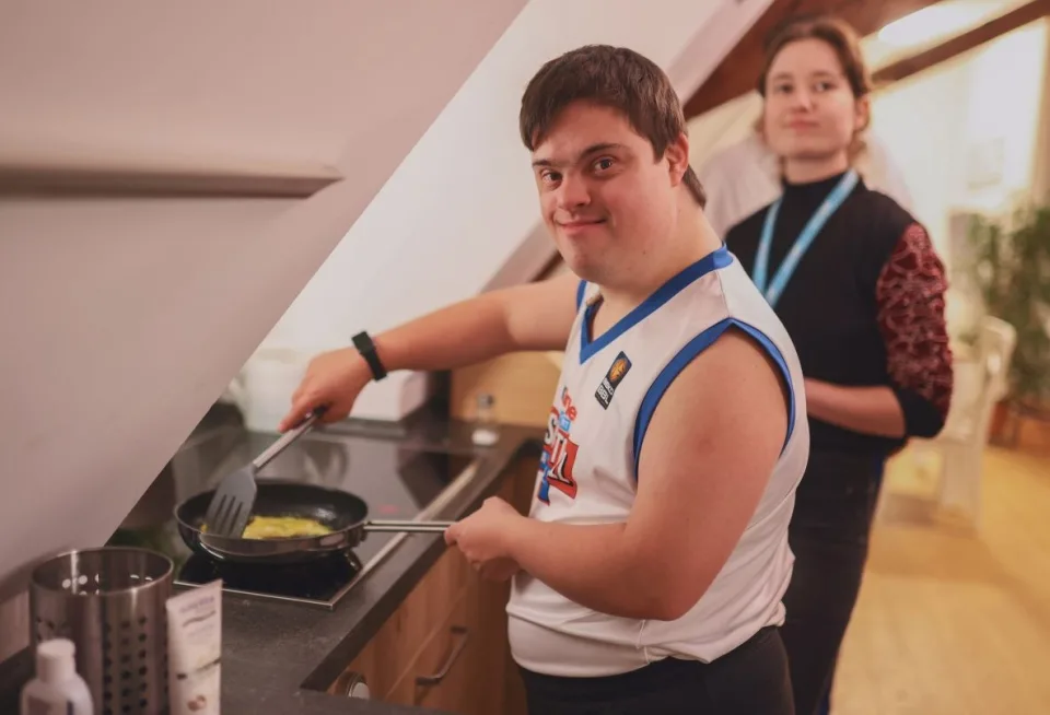 Ein junger Mann mit Downsyndrom brät etwas in einer Pfanne in einer Wohnung.