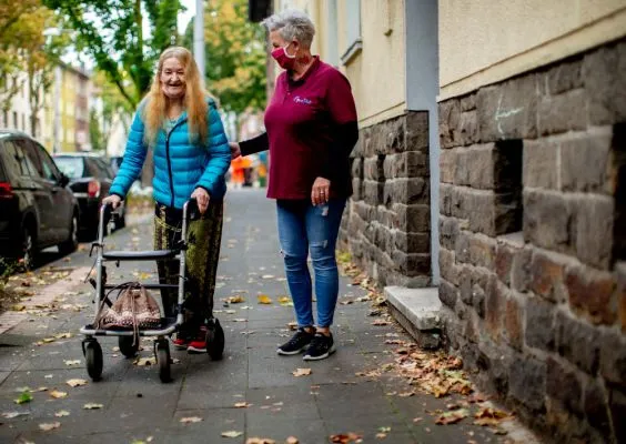 Eine Frau hilft einer anderen Frau, die mit einer Geh-Hilfe geht.