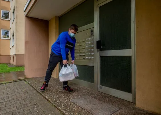 Ein junger Mann steht vor der Haustür eines Mehr-Familien-Hauses.