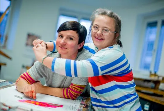 Eine junge Frau mit Down-Syndrom umarmt eine andere Frau.