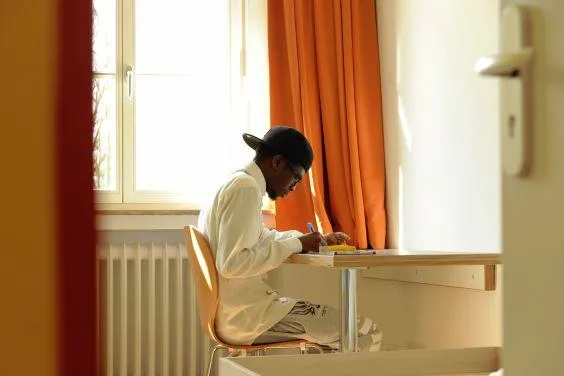Ein unbegleiteter minderjähriger Flüchtling sitzt in einem Zimmer an einem Schreibtisch.