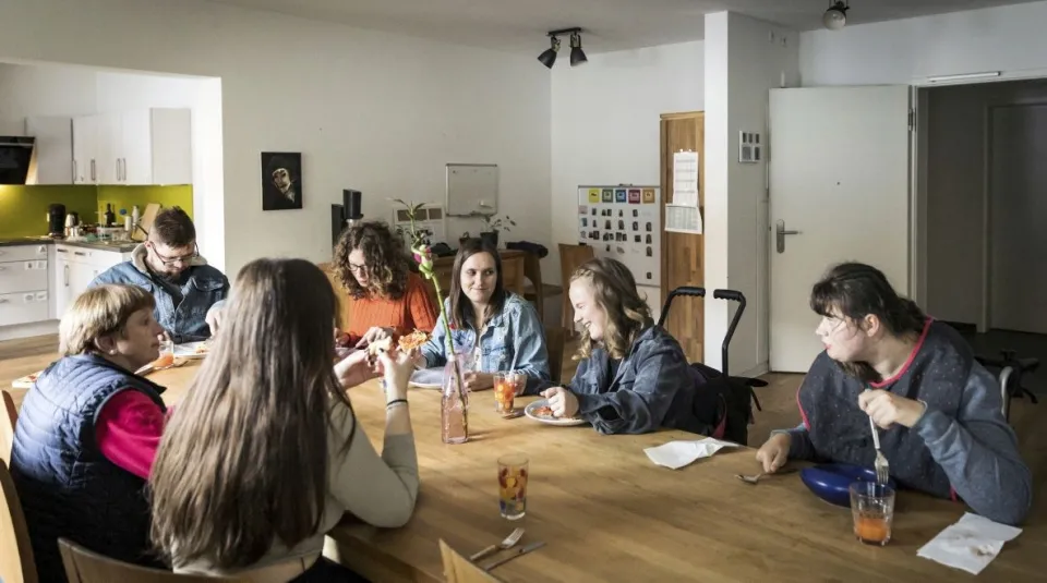 Menschen mit und ohne Behinderung sitzen an einem Tisch in einer inklusiven Wohngemeinschaft.