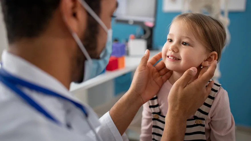 Ein Arzt Untersucht ein Kleinkind am Hals.