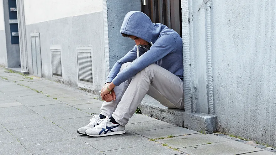 Ein Jugendlicher mit Kapuzenpulli sitzt traurig am Straßenrand