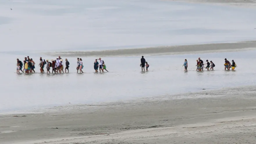 Eine Gruppe von Menschen, die in einer Entfernung durch ein Gewässer waten.