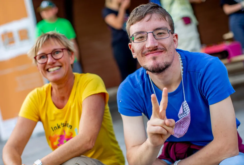 Ein Mann sitzt neben einer Frau und macht mit Hand ein Victory-Zeichen.