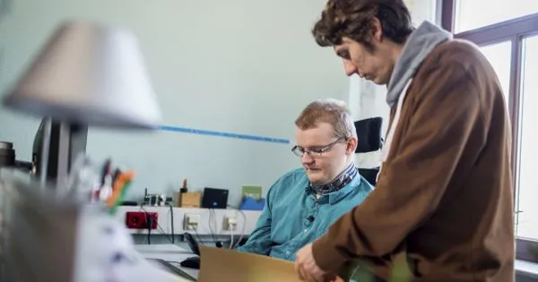 Ein Assistent hilft einem Mann mit Behinderung bei der Arbeit.