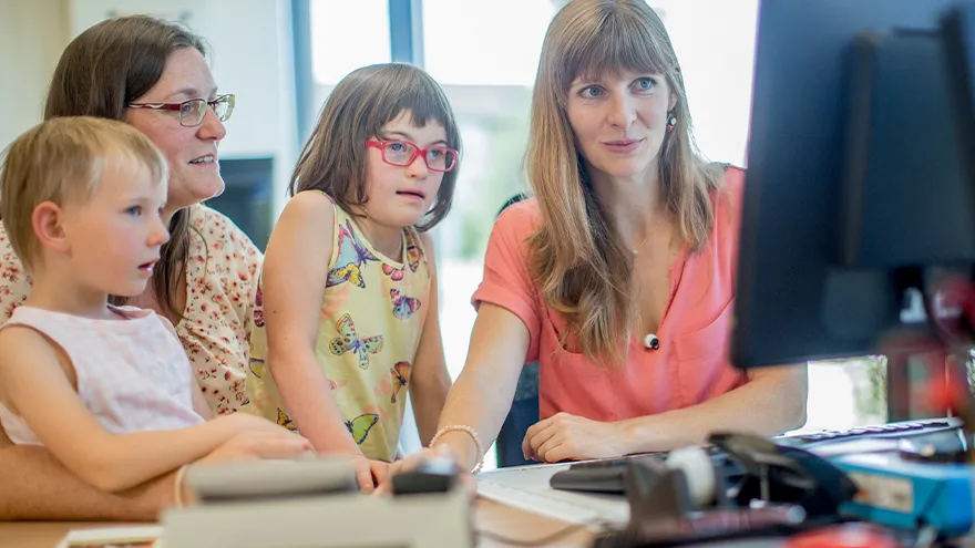 Zwei Frauen und zwei Mädchen (eines davon mit Down-Syndrom) vor einem Computer-Bildschirm