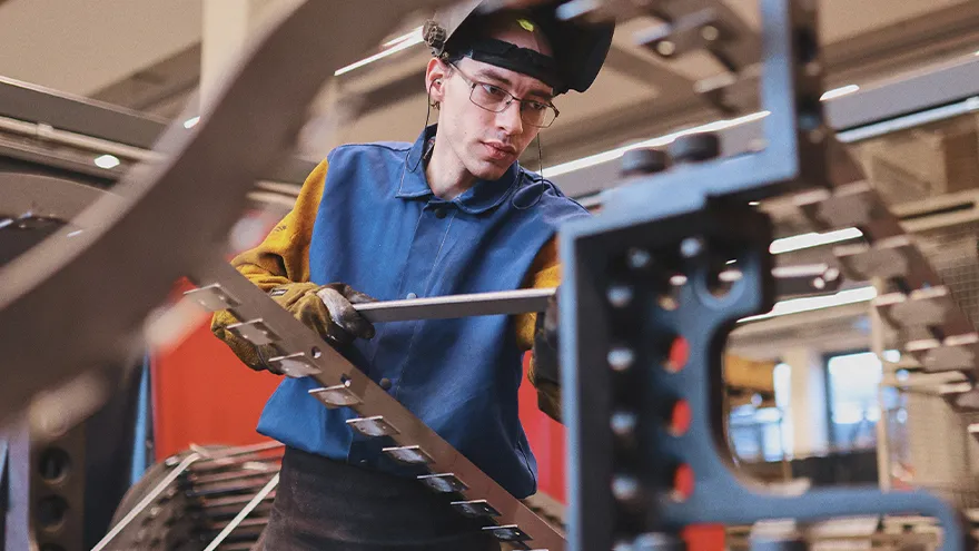 Ein junger Mann hat ein Werkzeug in der Hand und arbeitet an einer Maschine.