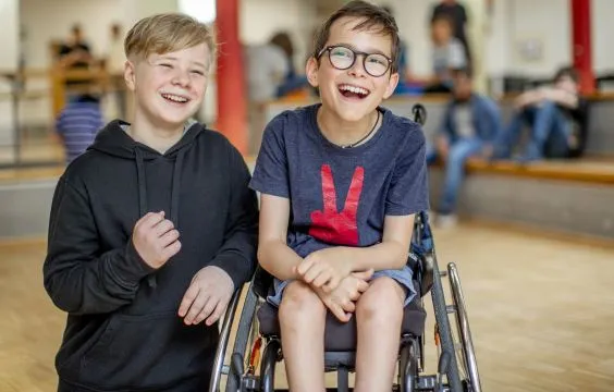 Zwei Jungs in der Schule, sie lachen, einer sitzt im Rollstuhl.