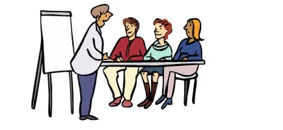 Eine Gruppe sitzt an einem Tisch, davor steht eine Frau und erklärt etwas.