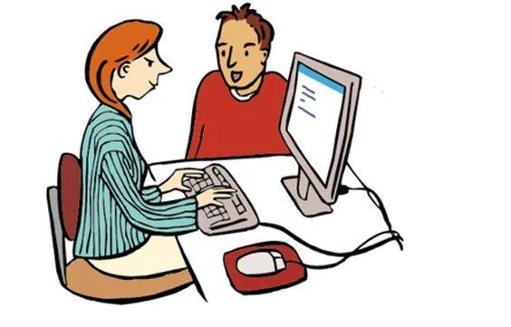 Eine Frau sitzt an einem Schreibtisch mit Computer. Daneben sitzt ein Mann auf einem Stuhl.