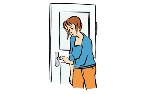 Eine traurige Frau steht an einer Zimmertüre und fasst die Klinke an.